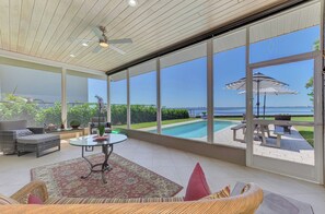 A sunlit room with a large window, a ceiling fan, and a view of a swimming pool and greenery. - Sarasota Sunset Villa-Luxury waterfront pool home (Sarasota)