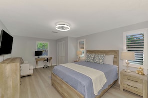 Een slaapkamer met een bed, nachtkastjes, een bureau, een televisie en een plafondlamp.