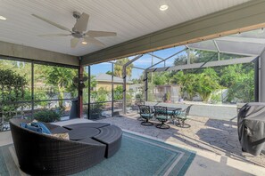 Eine überdachte Terrasse mit Deckenventilator, Korbmöbeln und Grill.