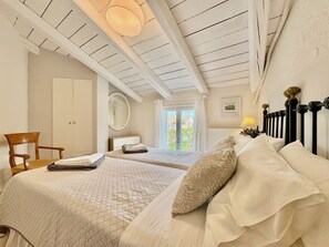 A bedroom with two beds, a chair, a mirror, and a window with curtains. - Villa Sweet Nest with private heatable pool (Kassiopi)