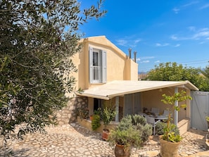 A Mediterranean-style house with a stone patio, potted plants, and a white table and chairs. - Villa Sweet Nest with private heatable pool (Kassiopi)