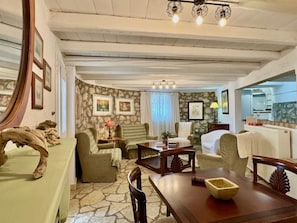A room with a stone floor, wooden furniture, a dining table, and a kitchen area visible through an archway. - Villa Sweet Nest with private heatable pool (Kassiopi)