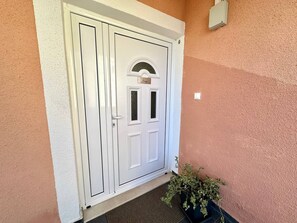 Uma porta branca com uma placa, um vaso de planta e um quadro de eletricidade fixado na parede.