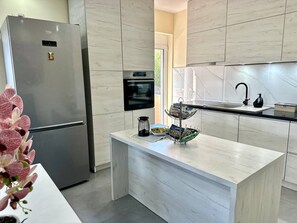 Uma cozinha moderna com geladeira de aço inoxidável, forno embutido e bancada de mármore.