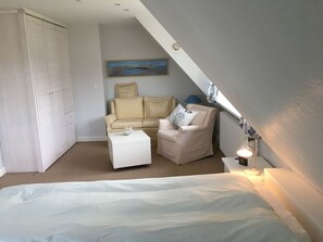 Ein Schlafzimmer mit einem Bett, einem Schlafsofa, einem Sessel, einem kleinen Tisch und einem Gemälde an der Wand.