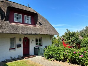A traditional thatched-roof house with a red door and white walls, surrounded by greenery. - Holiday Home Hochstieg 30 (Nieblum)