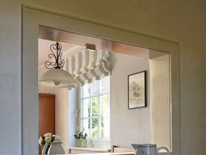 A room with a window, a hanging light fixture, a framed picture on the wall, and a vase with flowers on a table. - Holiday Home Hochstieg 30 (Nieblum)