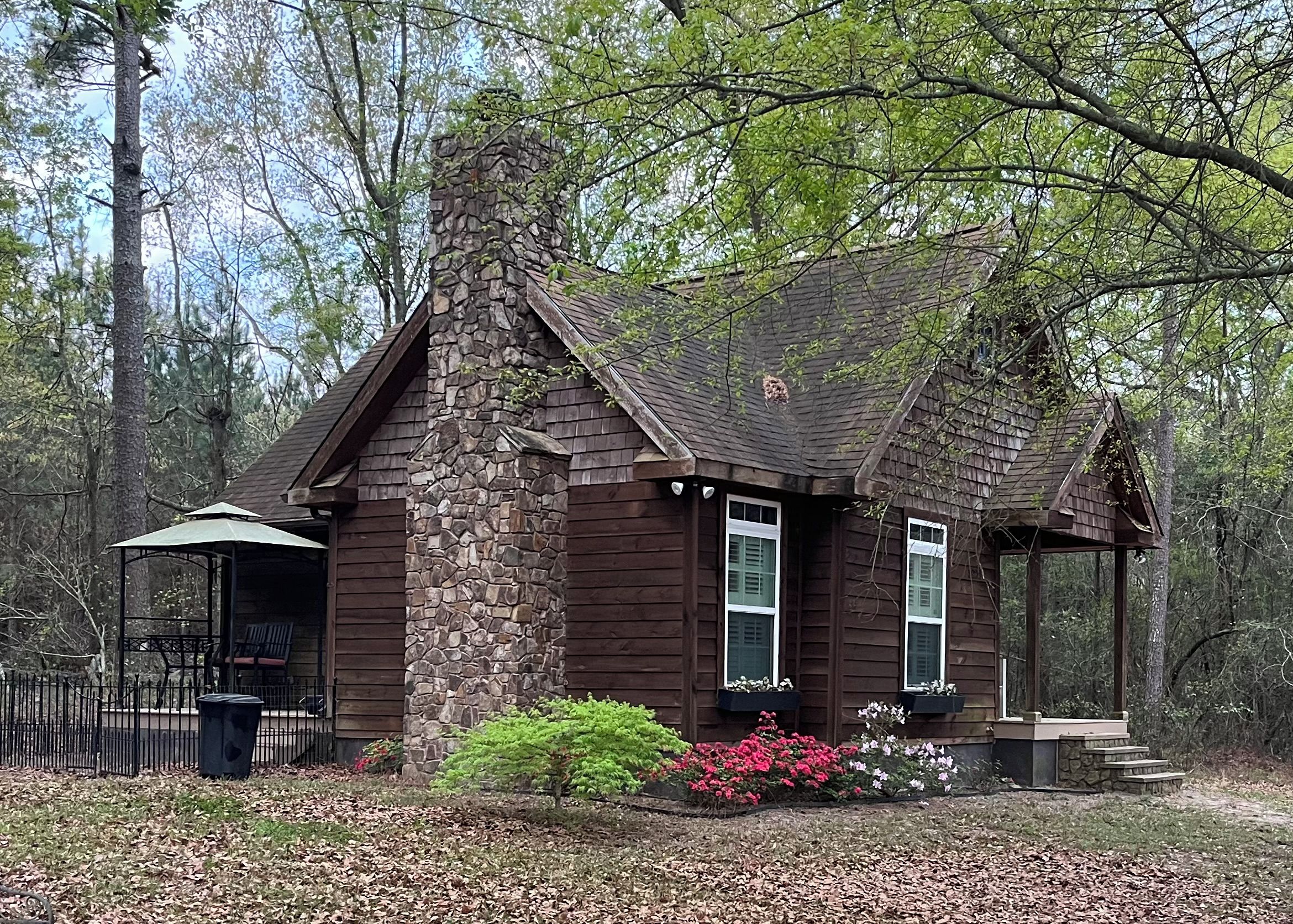 A rustic cabin with a stone chimney, wooden siding, and a porch.
