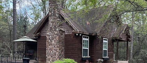 A rustic cabin with a stone chimney, wooden siding, and a porch.