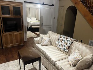Una sala de estar con un sofá, televisión, aparador y escalera.