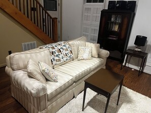 Ein beiges Sofa mit gestreuten Kissen, einer passenden Decke und zwei Zierkissen. Davor steht ein kleiner Holztisch.