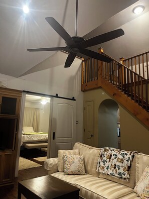 Una sala de estar con ventilador de techo, una escalera y una cama al fondo.