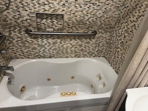Una bañera con pared de mosaicos, barra de apoyo y cortina de ducha.