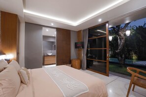 A modern bedroom with a large bed, a TV, and a sliding glass door leading to a balcony. - Family-friendly 4-Bedroom Villa with Private Pool (Badung)