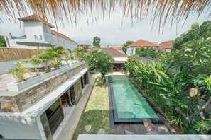 A pool area with a clear water surface, surrounded by lush greenery and a stone wall. - Family-friendly 4-Bedroom Villa with Private Pool (Badung)