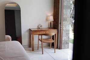 A room with a bed, a wooden desk with a lamp, and a stone wall. - Family-friendly 4-Bedroom Villa with Private Pool (Badung)