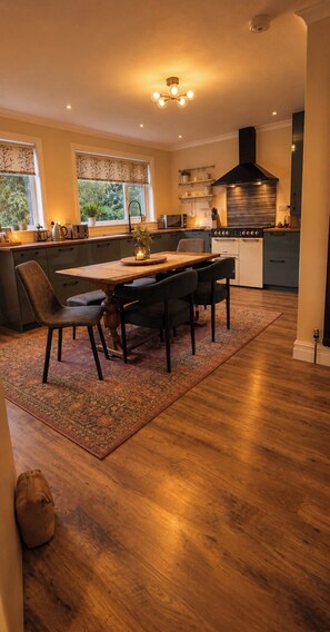 A modern kitchen with a dining area, wooden flooring, and a large window. - House Sleeps 6 by the Coast With Enclosed Garden (Fortrose)