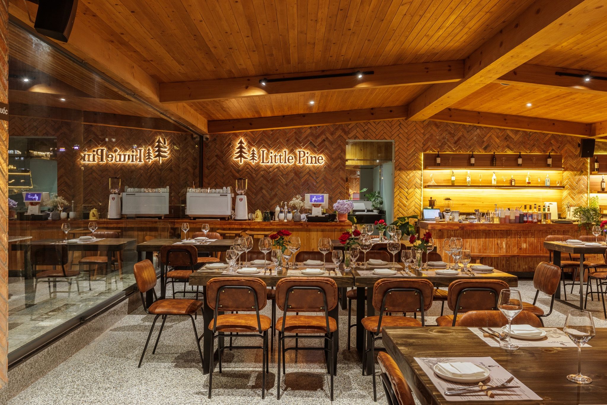 Interior de restaurante con paredes de madera, una zona de bar y mesas dispuestas para comer.