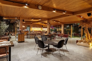 Un interior de restaurante con vigas de madera en el techo, mesas con sillas y una zona de bar.
