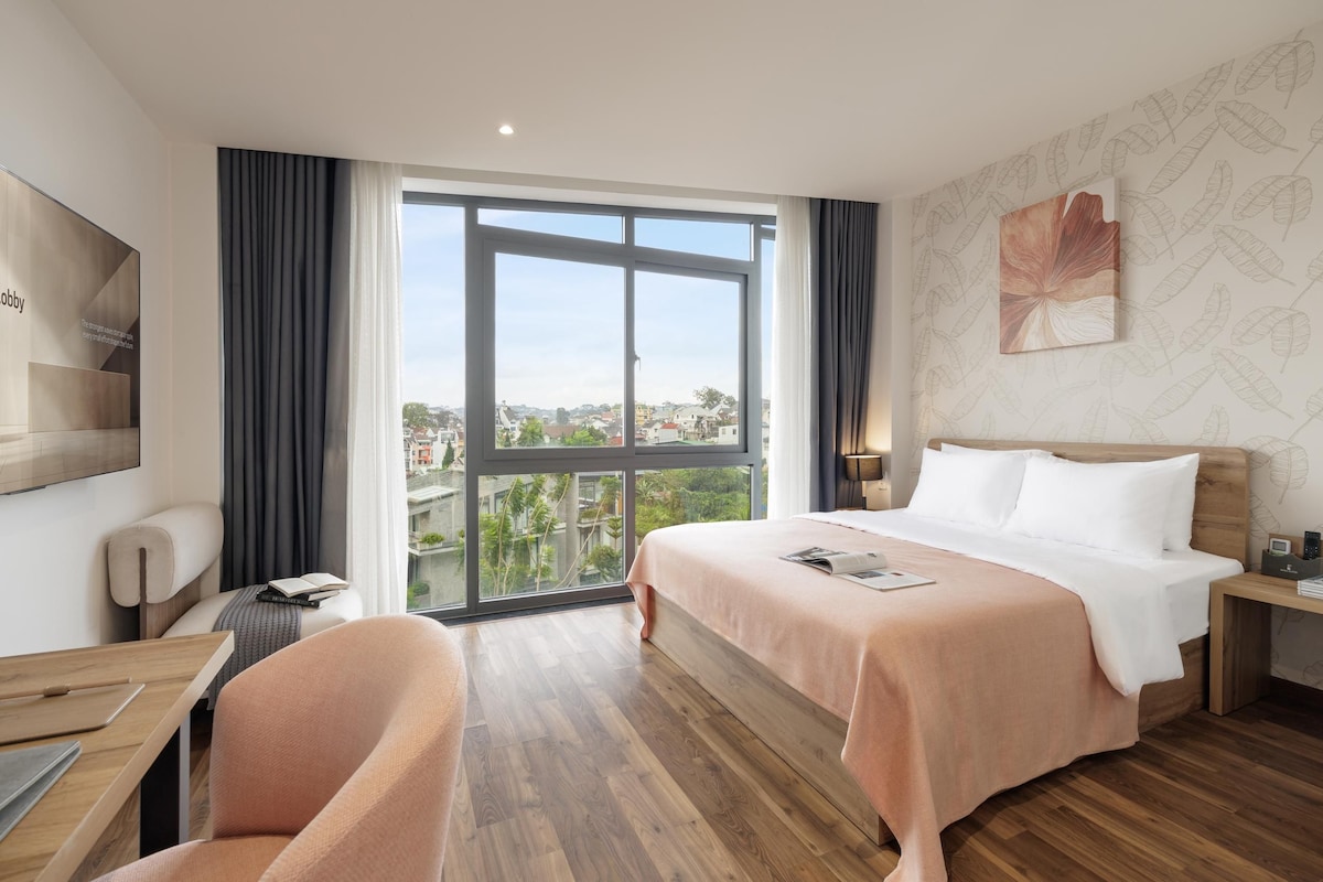 Een hotelkamer met een groot raam, een bed, een bureau en een stoel.