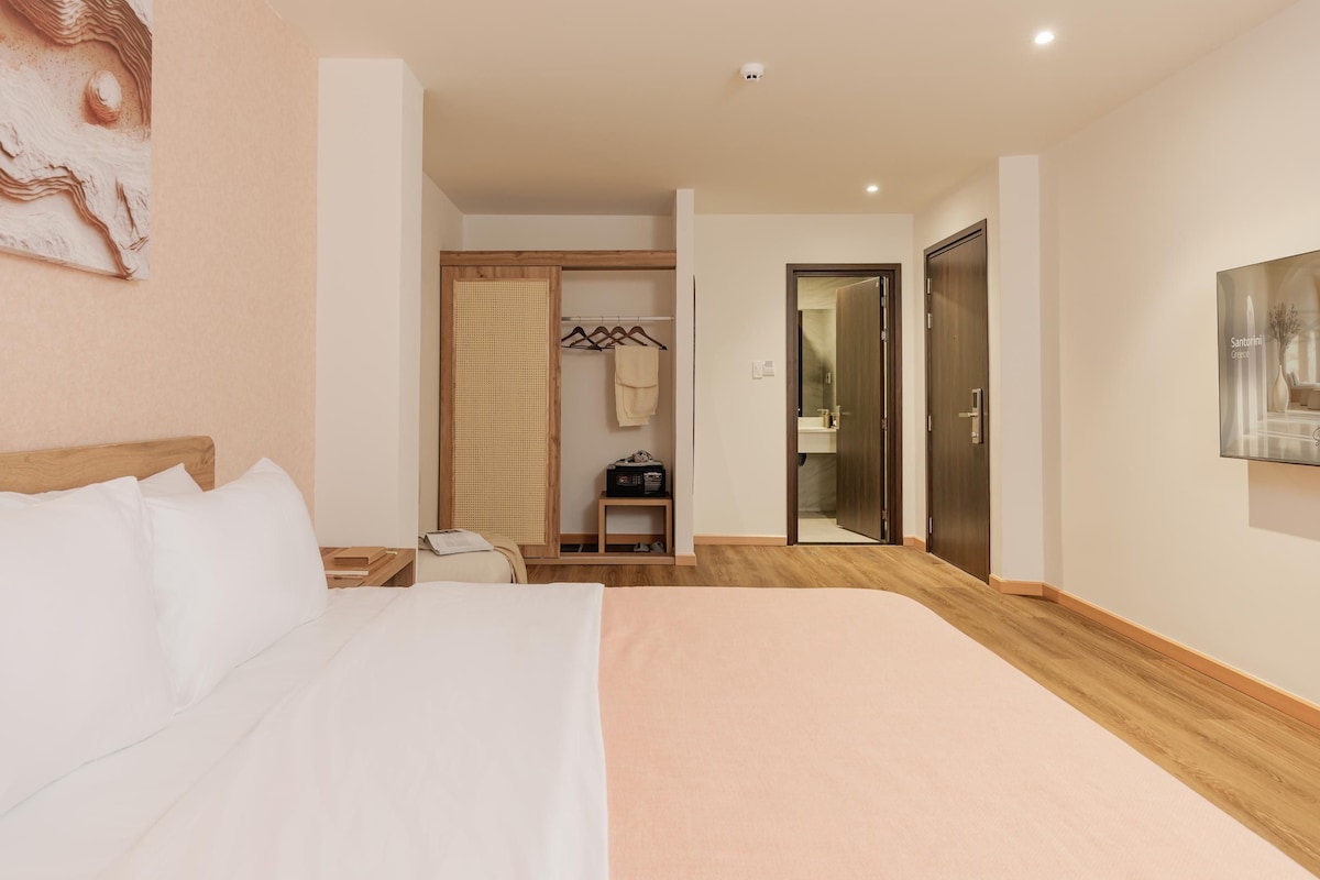 Een hotelkamer met een bed, een houten vloer, een kledingkast, een spiegel en een deur naar een badkamer.