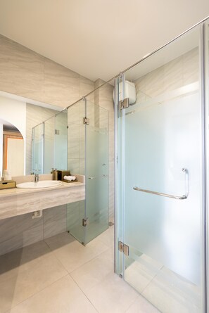 Un baño moderno con cabina de ducha de vidrio, tocador con lavamanos y un espejo grande.