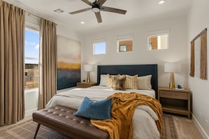 Une chambre à coucher avec un grand lit, un ventilateur de plafond, une vue sur l’extérieur et une fenêtre avec des rideaux.
