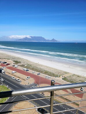A coastal road with vehicles, a beach, and a mountain in the background. - Perfect 2-bedroom apartment in Bloubergstrand for your getaway (Cape Town)