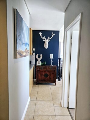 A hallway with a mounted deer head, a painting, a cabinet with decorative items, and a lamp. - Perfect 2-bedroom apartment in Bloubergstrand for your getaway (Cape Town)
