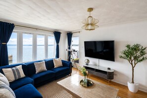 Een woonkamer met een modulaire bank, een flatscreen televisie, een potplant en uitzicht op de zee.