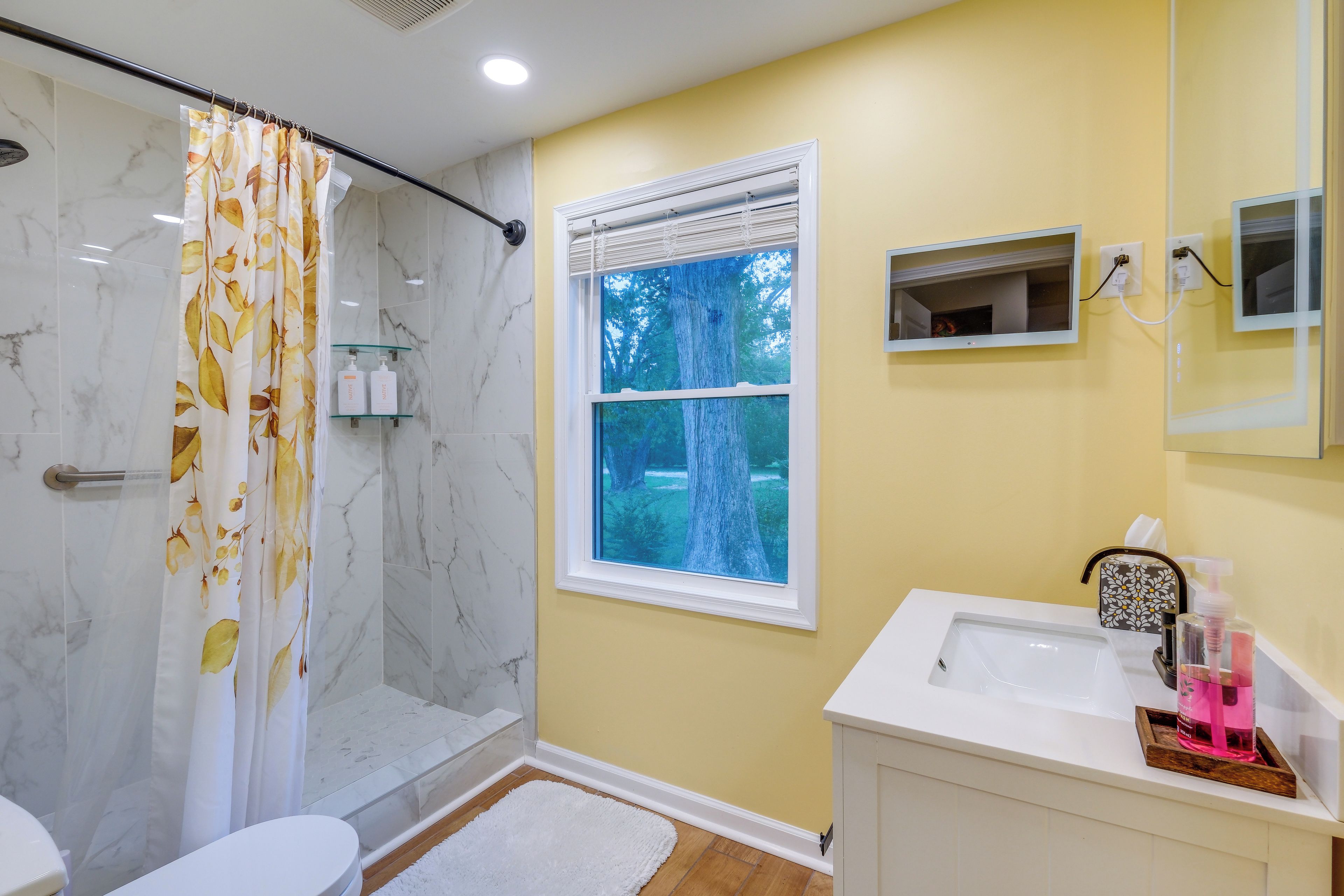 A bathroom with a shower, toilet, sink, and window with a view of trees.