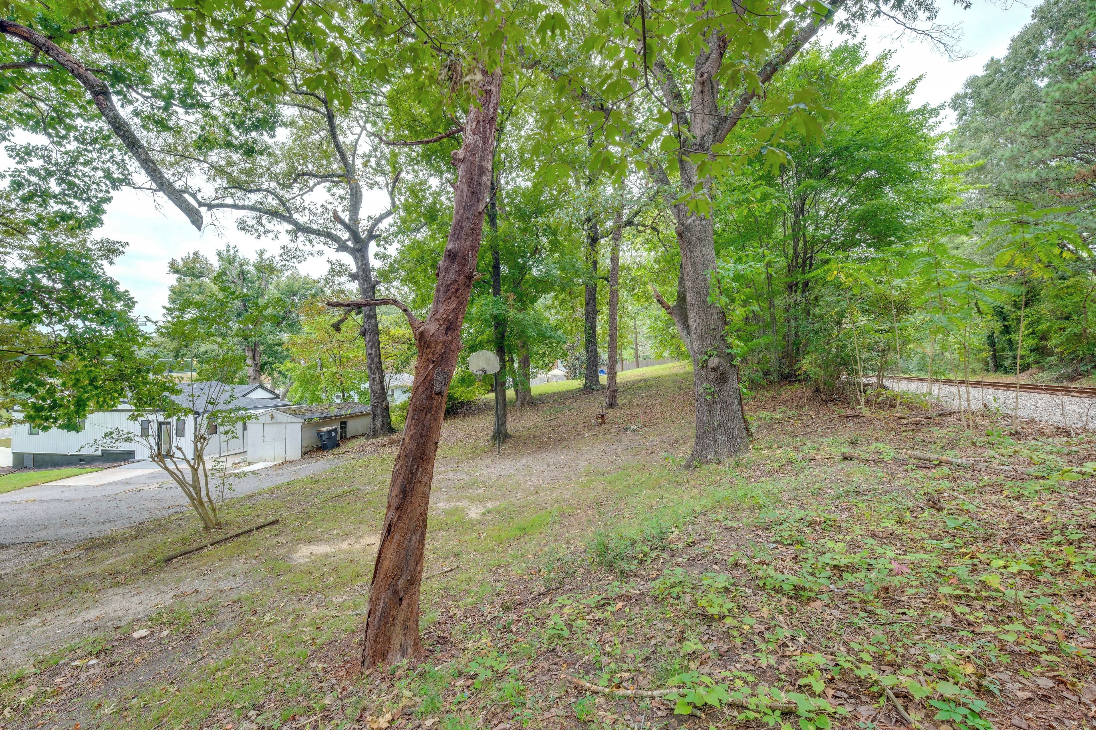 A wooded area with a white building, a dirt path, and a railway track.