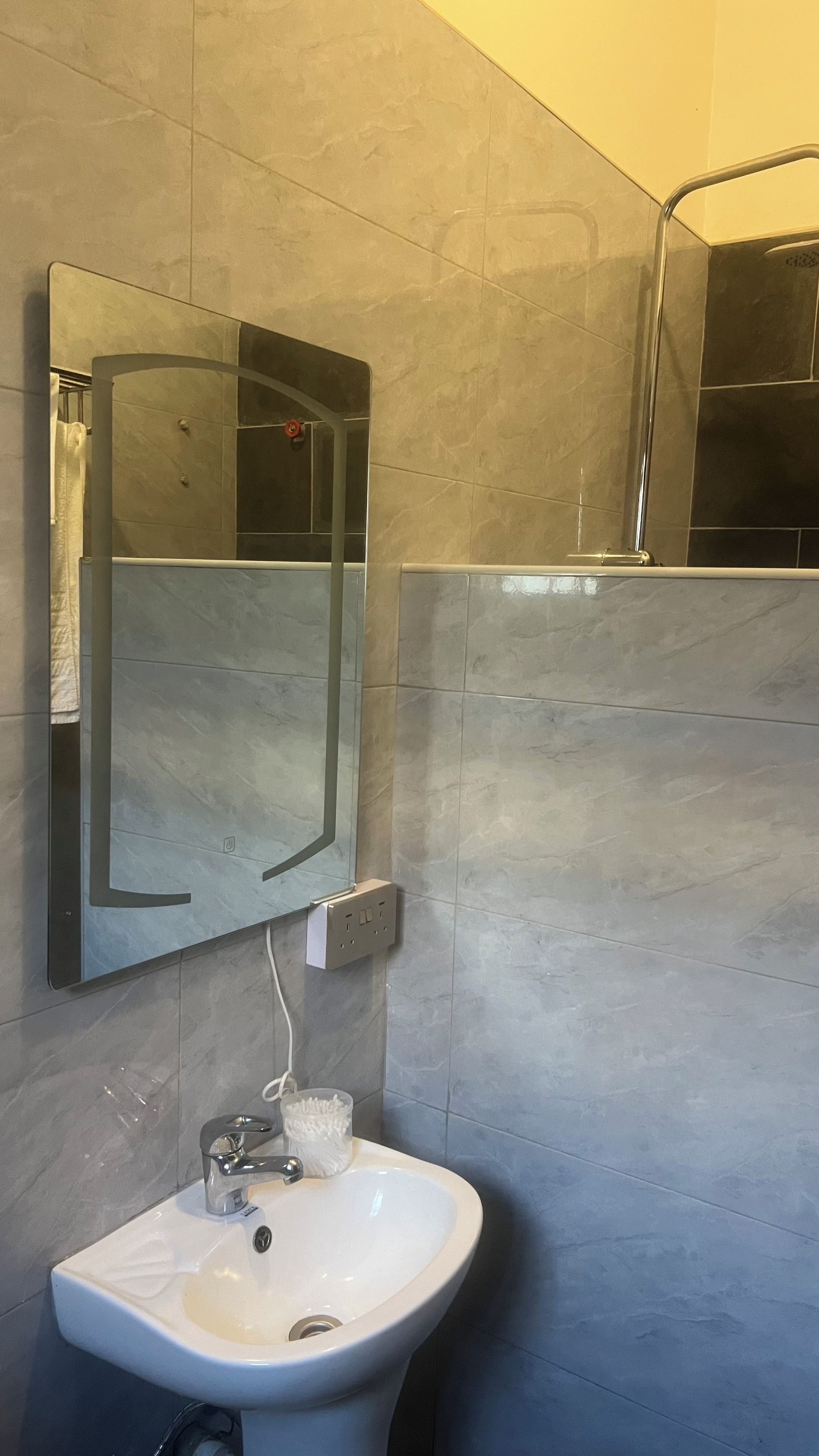 Een badkamer met een wit wastafelmeubel, een spiegel en een douchegedeelte.
