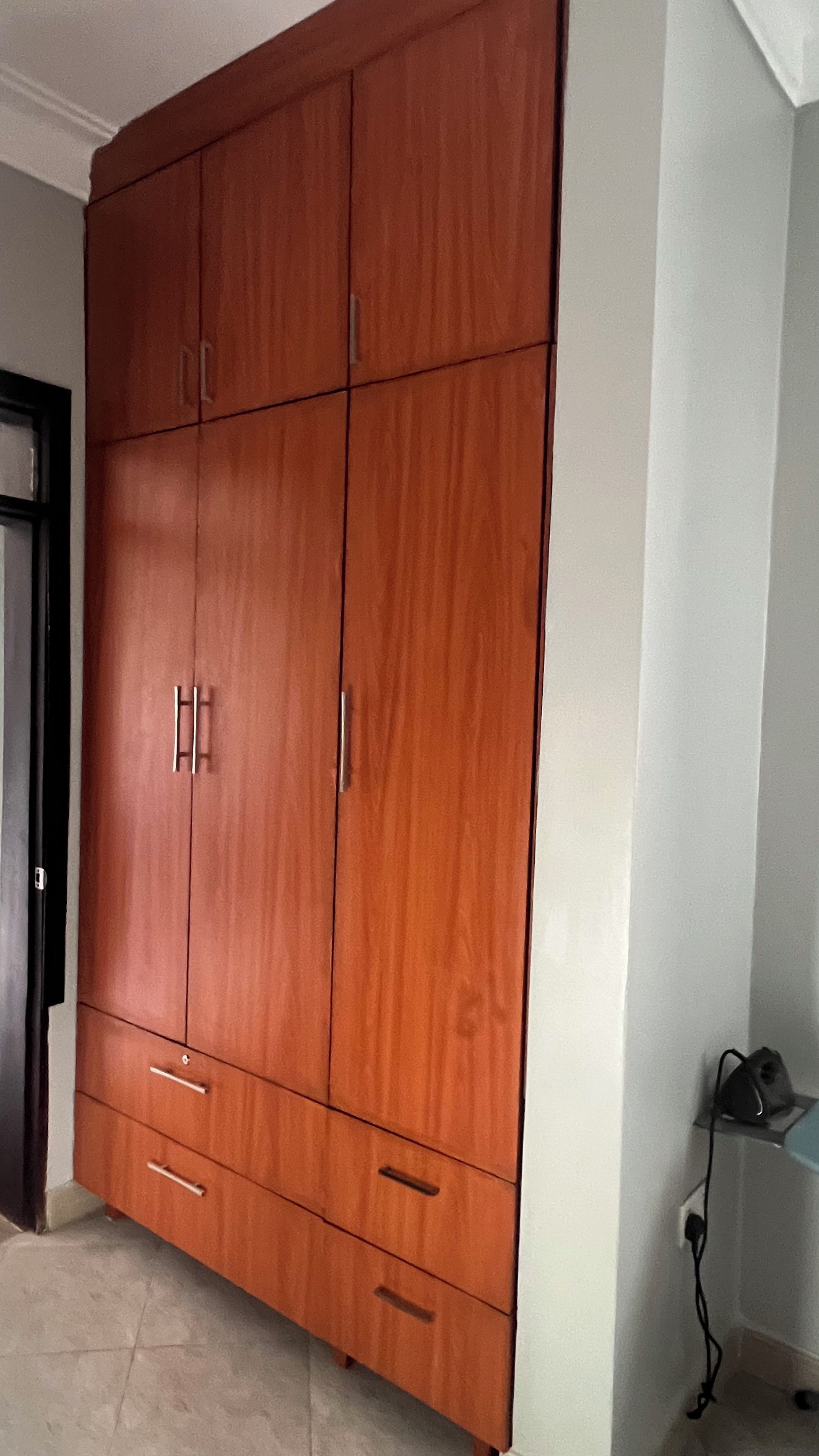 Une grande armoire en bois, dotée de nombreux tiroirs et de portes, un sol carrelé et une prise de courant au mur.