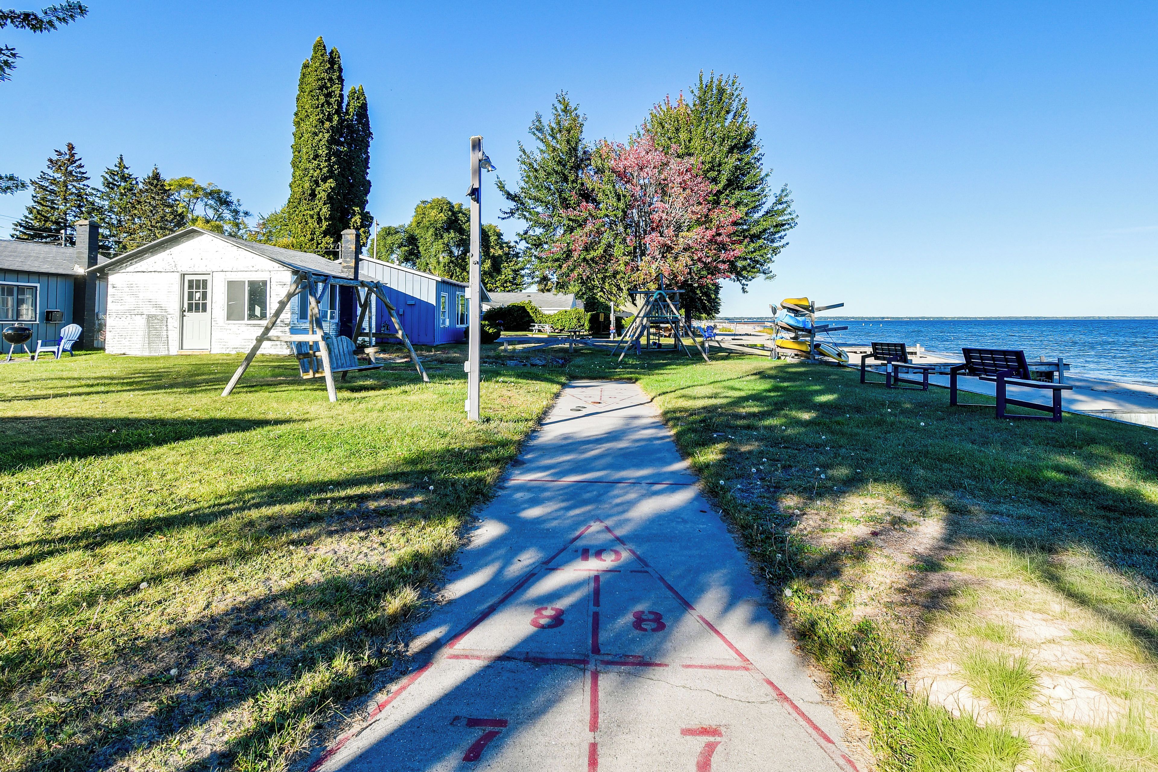 A clear path leading to a beach with a swing set and a small building.