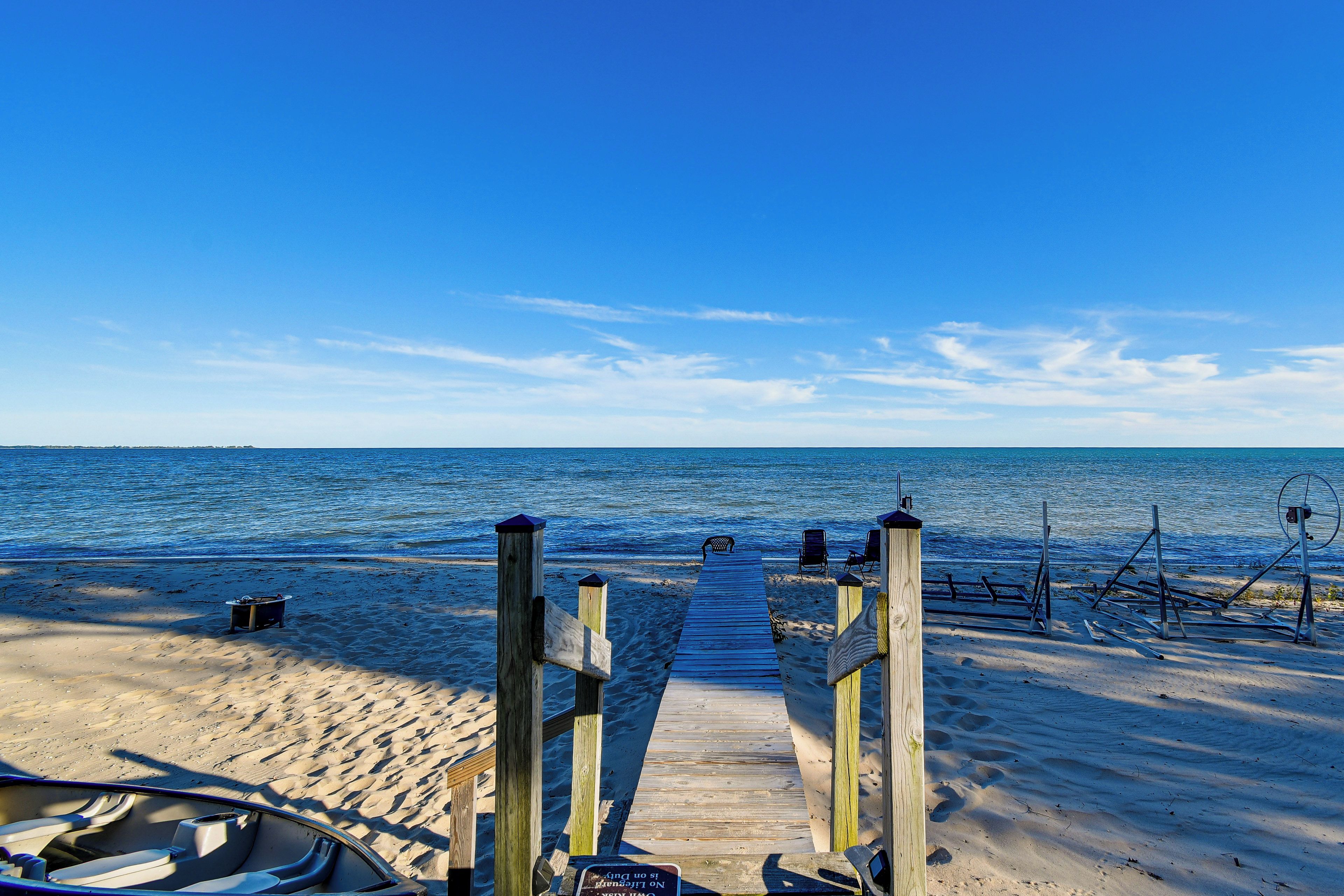 A wooden beach walkway leading to the ocean with beach chairs and a boat.