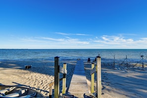 Une promenade en bois qui longe la plage et mène à l’océan, avec des chaises de plage et un bateau.