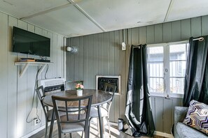 Une pièce avec un téléviseur fixé au mur, une table avec des chaises, une fenêtre avec des rideaux et un radiateur.