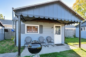 A small, single-story building with a porch, a barbecue grill, and three chairs. - Quaint Couples Unit w/ Lake Access in Tawas City (Tawas City)