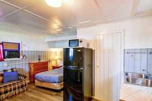 A compact room with a bed, a refrigerator, a microwave, a small sink, and a radio. - Quaint Couples Unit w/ Lake Access in Tawas City (Tawas City)