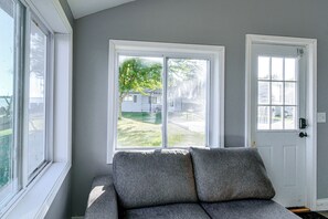 Ein Zimmer mit einem grauen Sofa, einer weißen Tür und einem Fenster mit Blick auf ein Haus und Grünflächen.