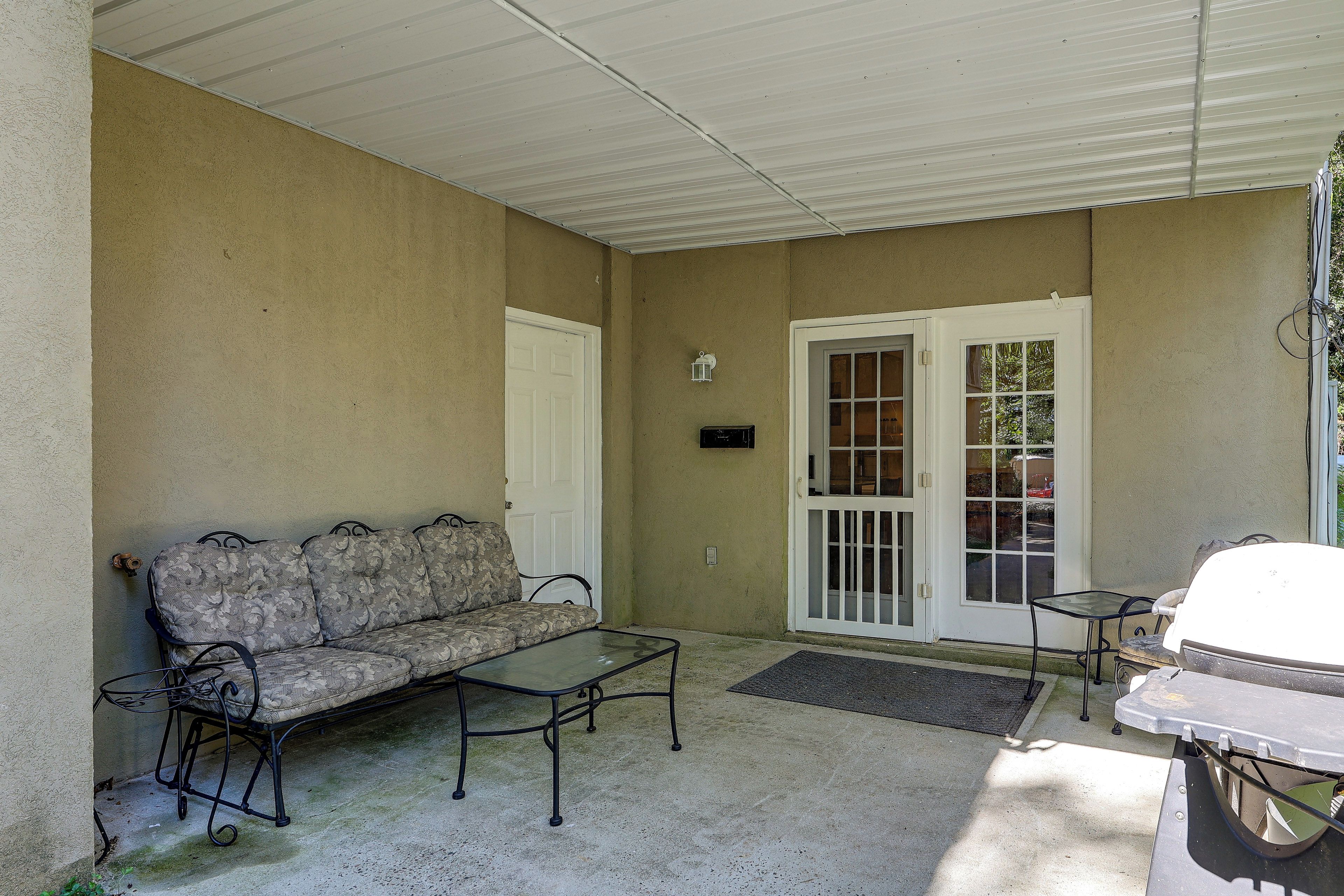 A covered patio area with a sofa, a small table, and a chair.