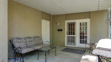 A covered patio area with a sofa, a small table, and a chair.