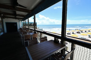 A beachside restaurant with wooden tables and chairs, a view of the ocean, and beach umbrellas. - Pool Access, Walk to Beach! Cape Canaveral Apt (Cape Canaveral)