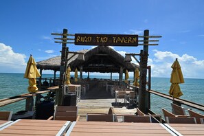 A wooden pier leading to a thatched-roof structure with a sign reading 'RKKI TIKI TAVERN'. - Cape Canaveral Getaway w/ Pool - Walk to Beach (Cape Canaveral)