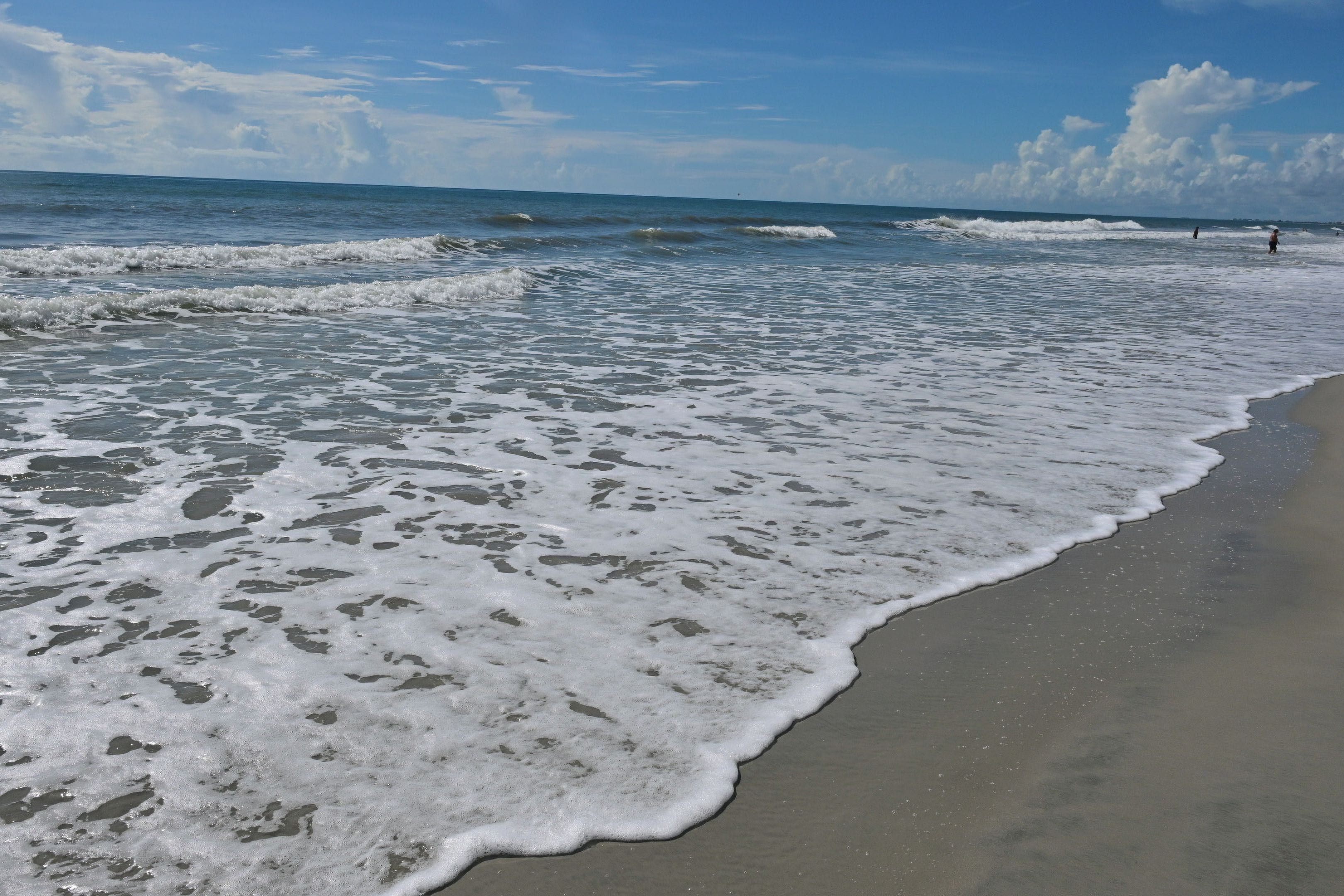 A beach with waves gently lapping onto the shore, a clear sky, and a distant horizon.