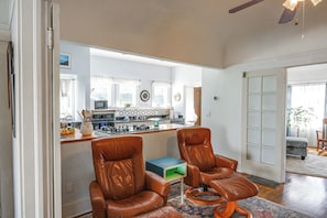 A spacious living room with a kitchen in the background, featuring leather chairs, a coffee table, and a view of the kitchen. - Jastro Park-facing 1922 Condo in Bakersfield (Bakersfield)
