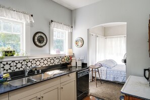 Eine Küche mit Spüle, Herd und Schränken, ein Essbereich mit Tisch und Stühlen sowie ein Schlafzimmer mit Bett und Vorhängen.