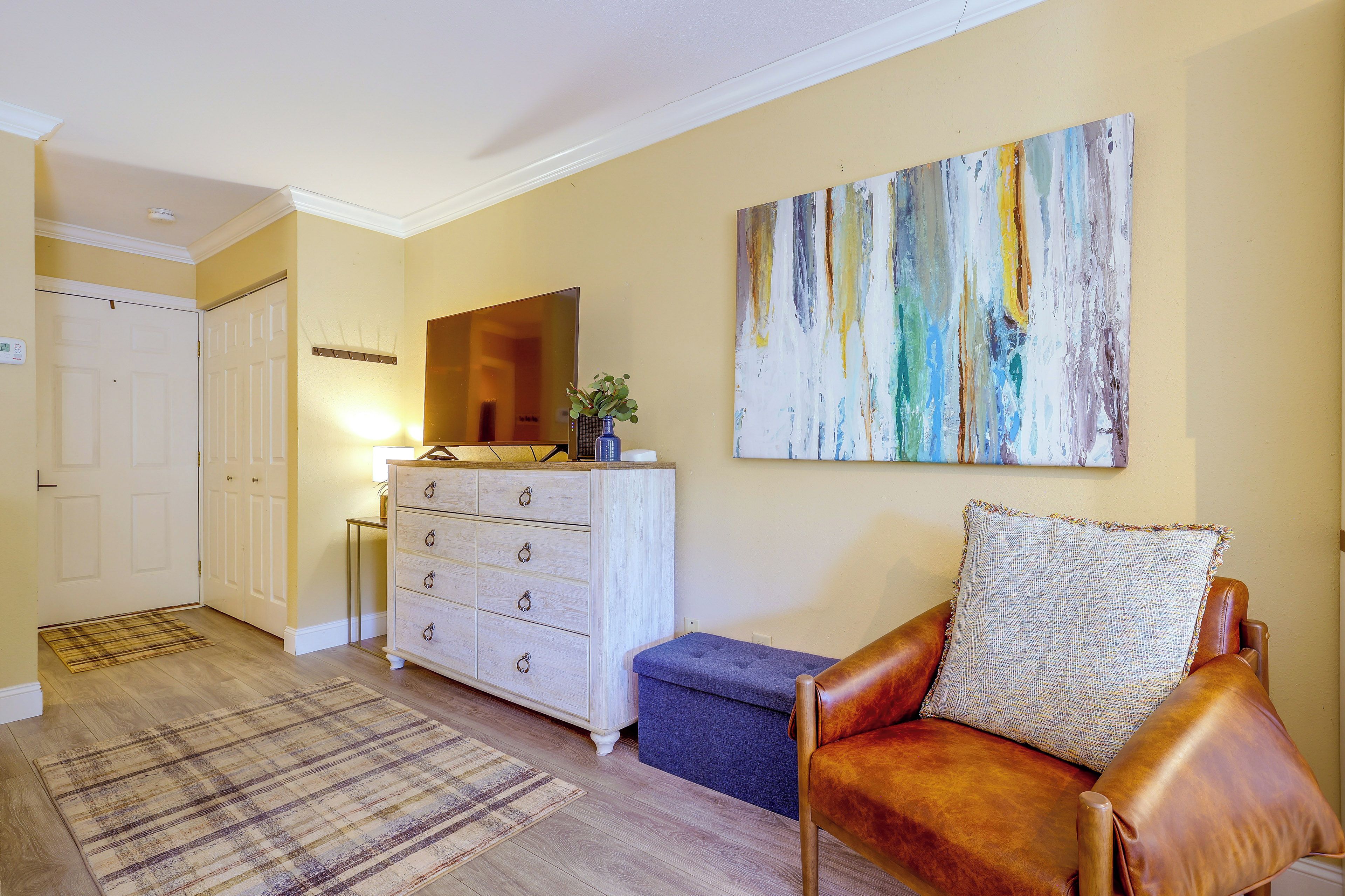 A living room with a sofa, a coffee table, a painting on the wall, and a door leading to another room.