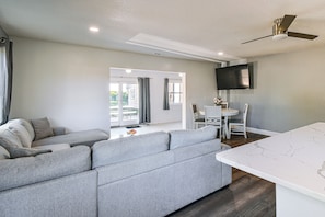 Ein modernes Wohnzimmer mit grauem Sofa, einem Esstisch mit Stühlen, einem flachbildfernseher an der Wand und einem Deckenventilator.